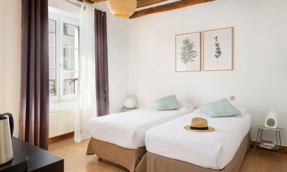 This is an image of a small bedroom with two single beds in the centre. It is very minimalistic and has a small wall with art.