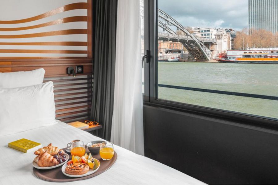 This is an image of a hotel room with a view of the Seine. There is also a big breakfast on the bed.