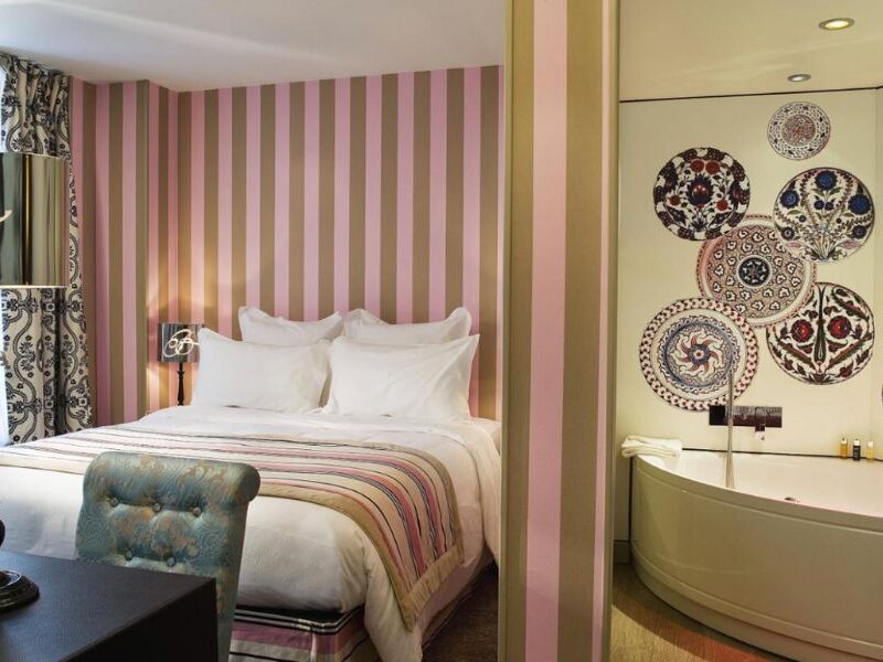 This is an image of a minimalist hotel room with beautiful art on the walls and a double room with pink stripy walls.