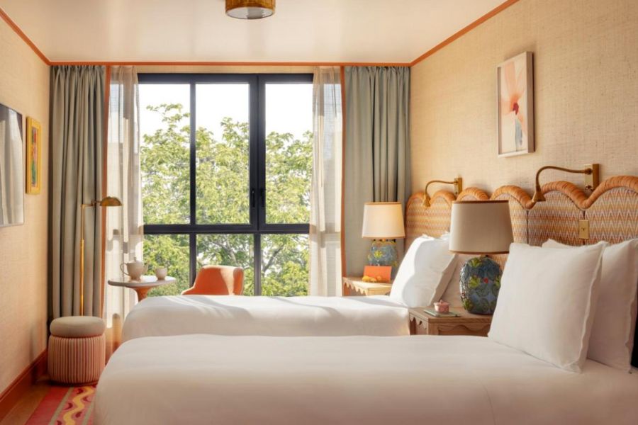 This is an image of a minimalist hotel room with lots of light coming through the windows and two beds.