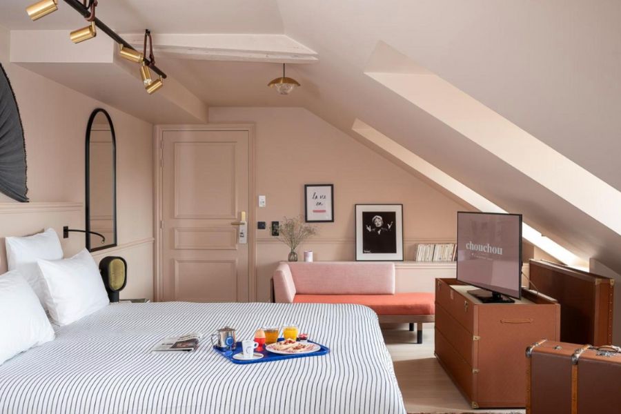 This is a picture of a minimalist room full of fun decor like a pink couch and contemporary poster art. The bed sheets are also stripy.