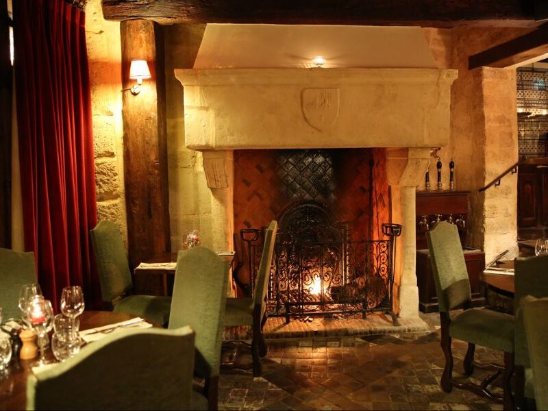 This is an image of a restaurant with old regal furniture, candles on tables and an open fireplace.