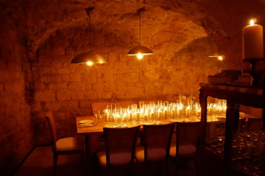 This is an image of a cozy cave room with a long table and candles all over it. The light is quite dark.