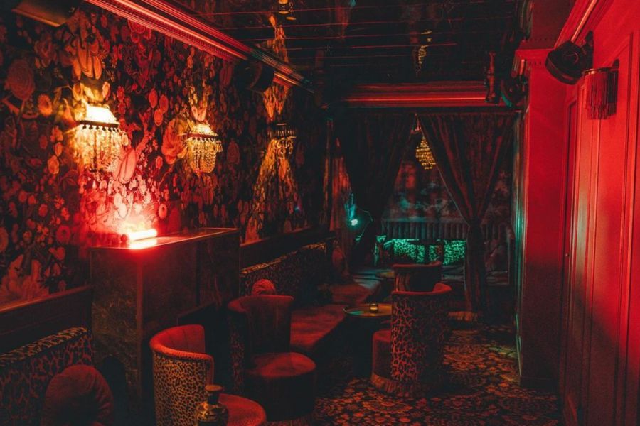 This is an image of a low-lit cocktail bar with very regal, patterned furniture and red feature lights.