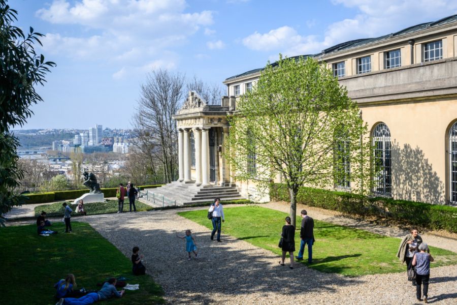 This is an image of a big castle-like structure with a few trees in front and people milling about.