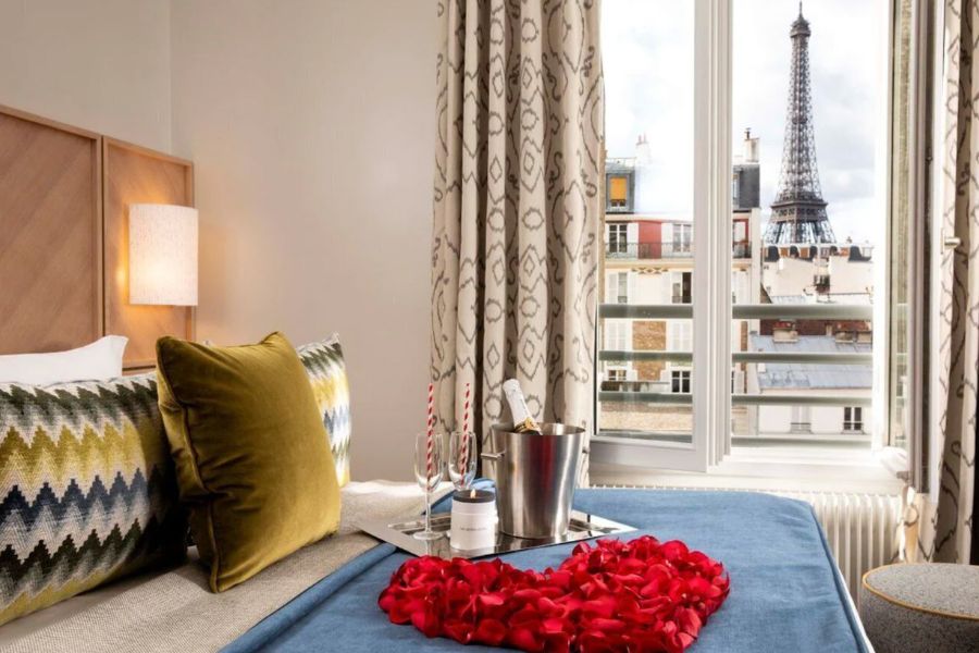 This is an image of a lovely hotel room with a view of the Eiffel Tower. There are also roses on the bed with wine and champagne.