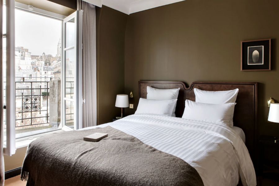 This is an image of a clean and neat hotel room with minimalist bedding and deep brown wall and decor features.