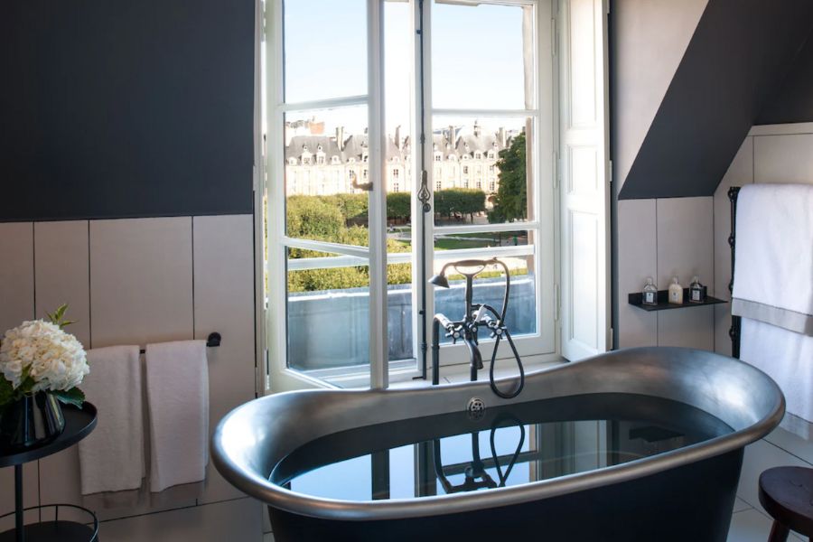 This is an image of a minimalist stand-alone bathtub overlooking a green, leafy Parisian street.