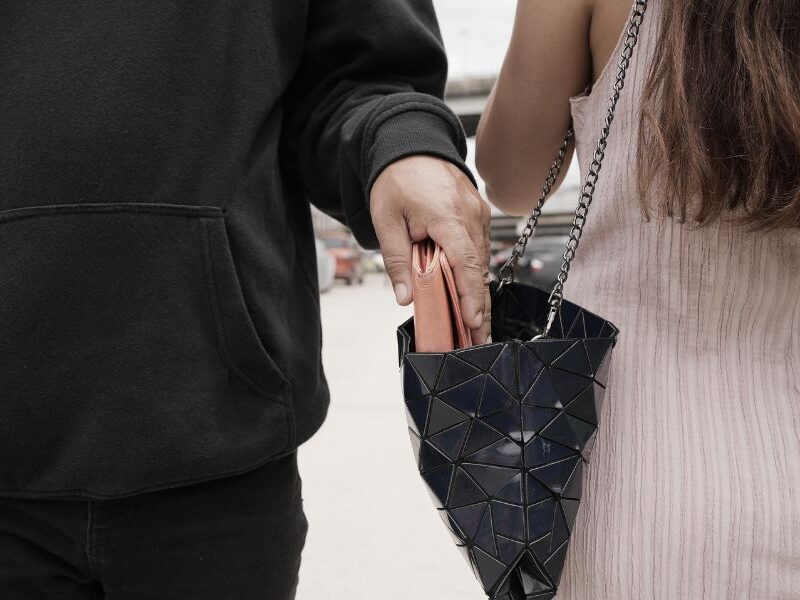 This is an image of a lady wearing a cross body bag and a man coming and taking her purse out of it.