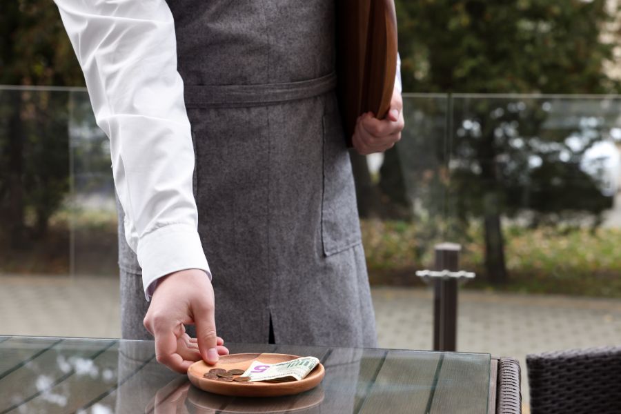 This is an image of a waiter picking up a plate with tips in it.