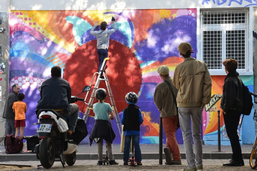 A crowd of adults and children watching a street artist painting a large colourful mural on a building wall, Paris