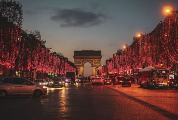 This is an image of the Arc de Triomphe with trees lining the street leading up to it, which are all dressed with red Christmas lights.