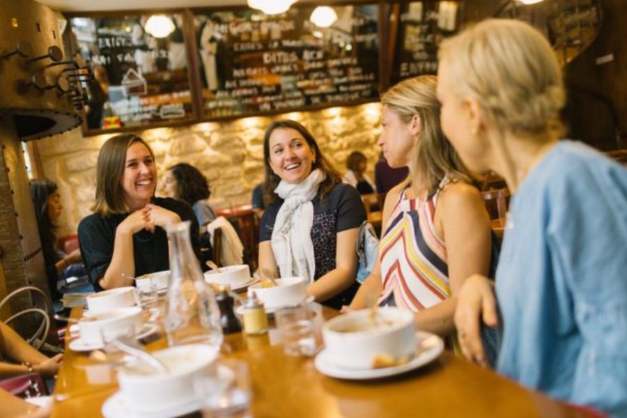 This is an image of a group of friends talking together over food at drink at a table in a restaurant or cafe.