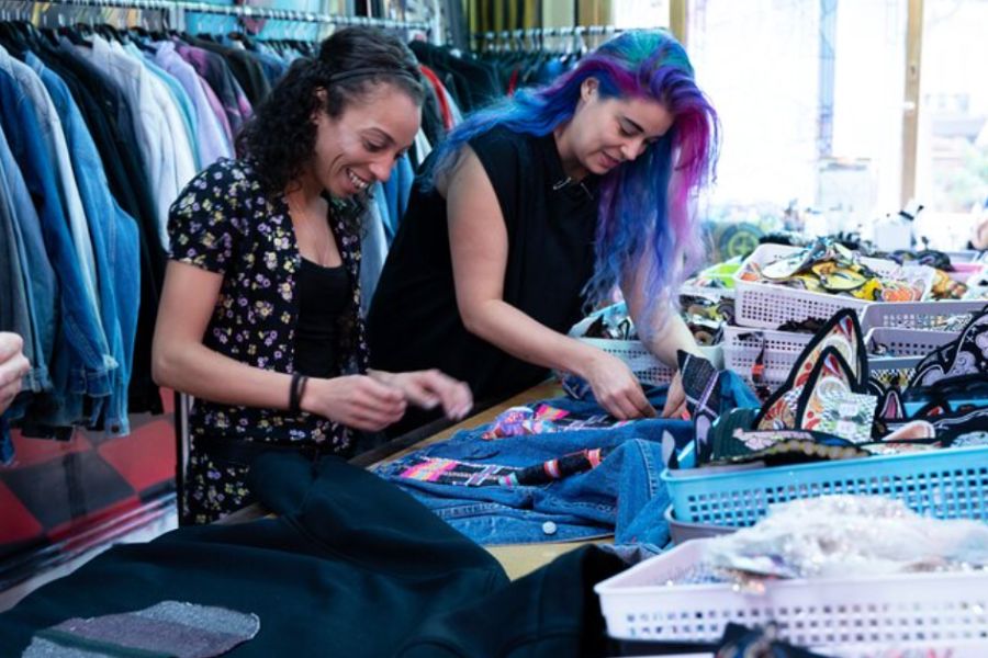 This is an image of two ladies decorating denim jackets at a crafty table smiling.