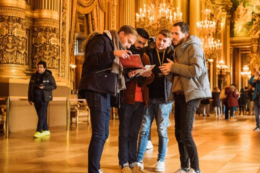 This is an image of a tour group reading clues in the middle of Palais Garnier huddled together.