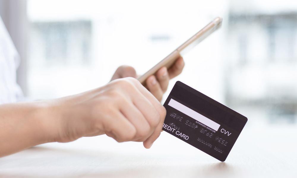 This is an image of someone holding a credit card while looking on their phone.