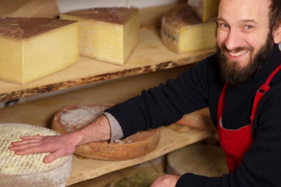 This is an image of a man sitting in front of a selection of homemade cheeses smiling proudly.