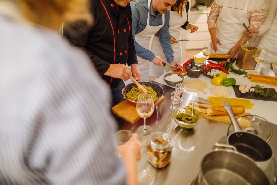 This is an image of a few people cooking together with glasses of wine.