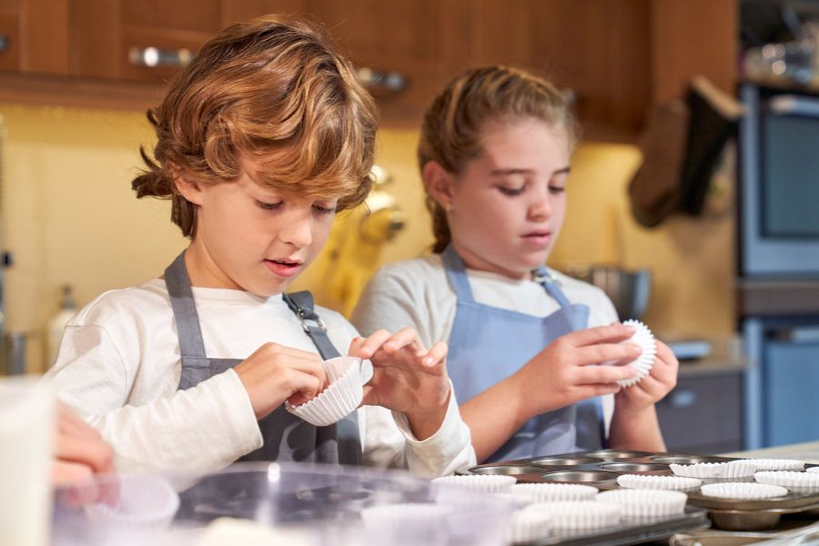 This is two kids putting muffin trays into baking tins.