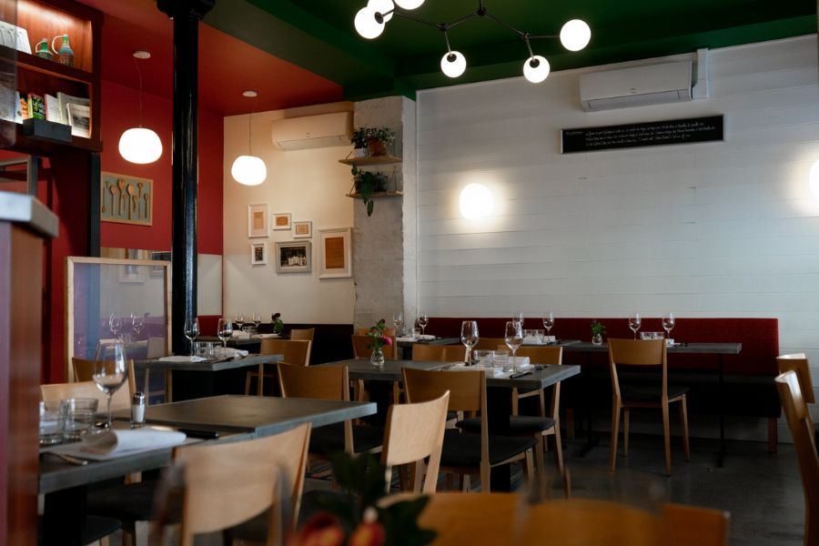 This is an image of a mood-lit restaurant with lots of minimalist tables and red wall accents with contemporary art.