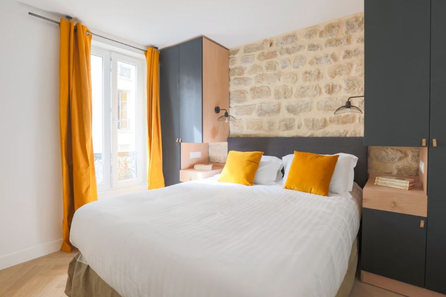 This is an image of a minimalist hotel room with a double bed and a pop of yellow curtains and pillows.