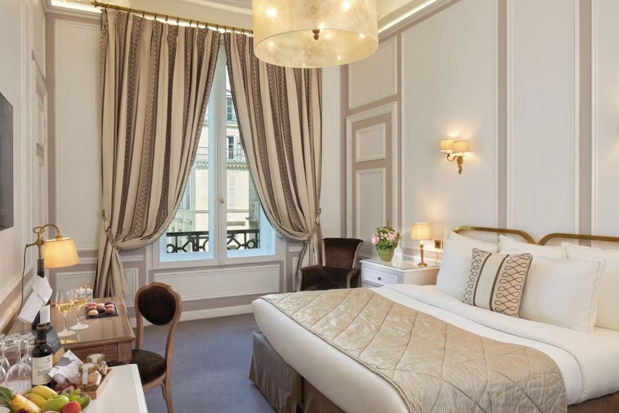 This is an image of a deluxe hotel room with nice royal fittings like gold decor and soft cream quilts and curtains.