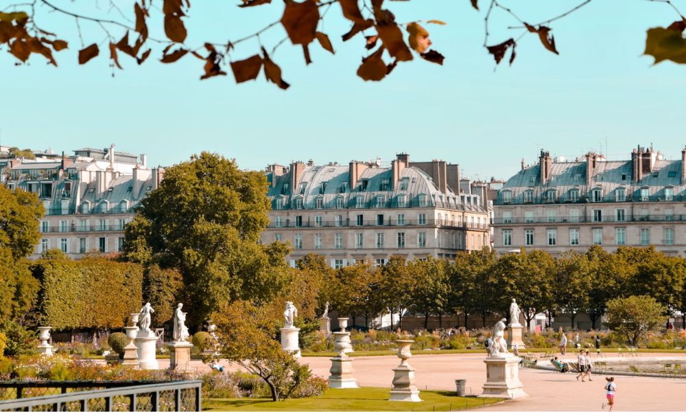 This is an image of Tuileries Garden with a bunch of statues and the Louvre buildings in the background.
