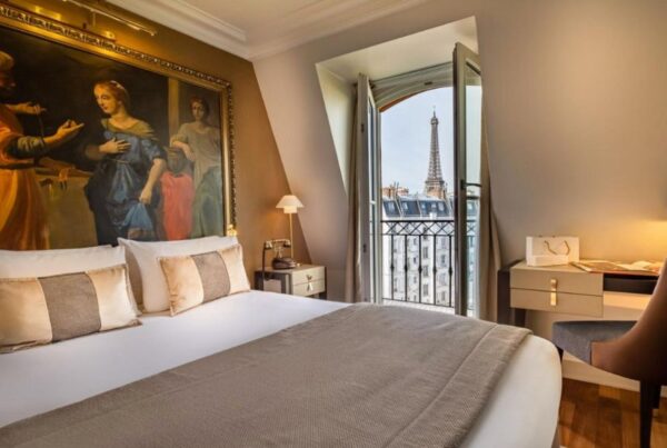 This is an image of a beautiful and large hotel room with a view of the Eiffel Tower and a classic French balcony.