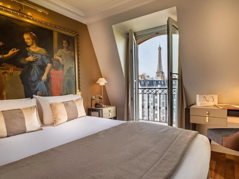 This is an image of a beautiful and large hotel room with a view of the Eiffel Tower and a classic French balcony.