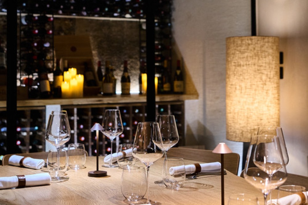 A table laid with wine glasses, with a large wine shelf behind it.