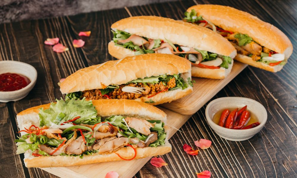 This is an image of a bunch of filled banguettes laid on a chopping board with chilli and sides.
