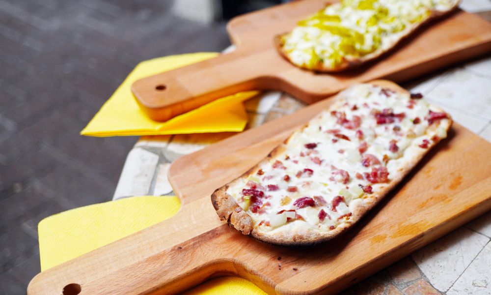 This is an image of two little trays of thin bread with pizza cheese and toppings.
