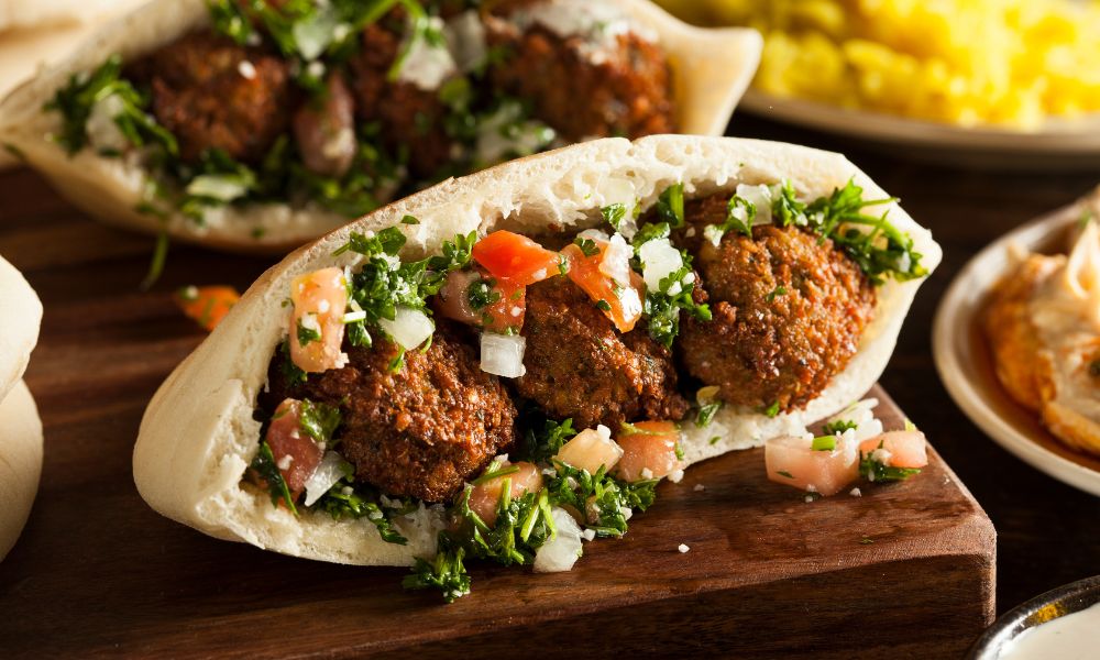 This is an image of a falafel pita laid out on the chopping board overfilling with fresh ingredients.