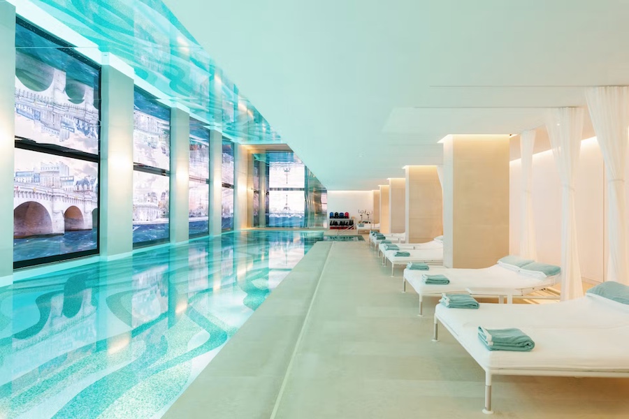 The picture shows a soft blue long pool, with white sun-chairs next to it.
