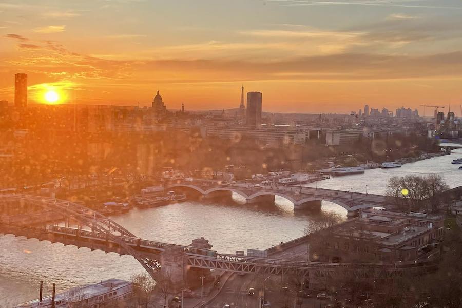 This is an image of Paris from a rooftop with views of the Seine and its surrounds with a beautiful orange sunset behind it.