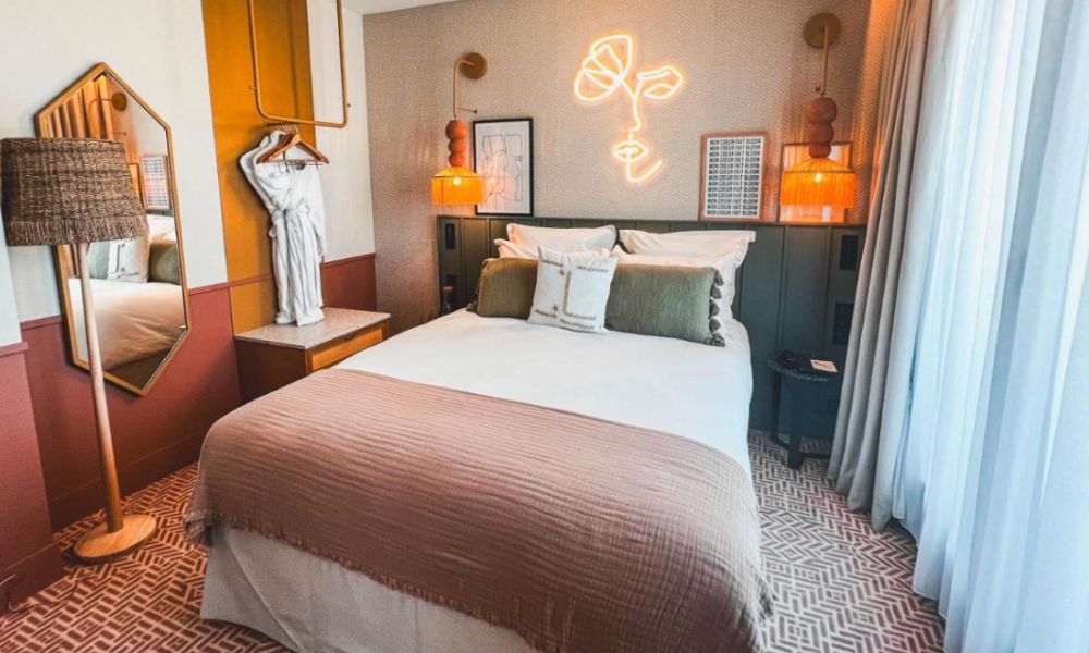 This is an image of a tidy and clean hotel room with a double bed, mirror and lamp. There's also plenty of art and cute decor pieces around, too.
