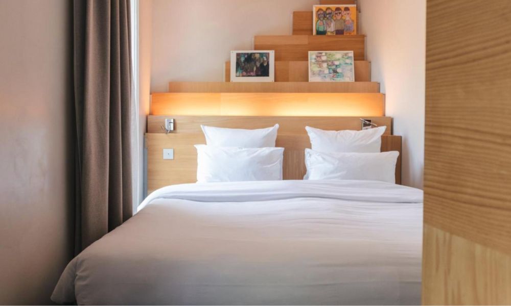 This is an image of a minimalist hotel room with white bed sheets and a bead head with built-in storage.