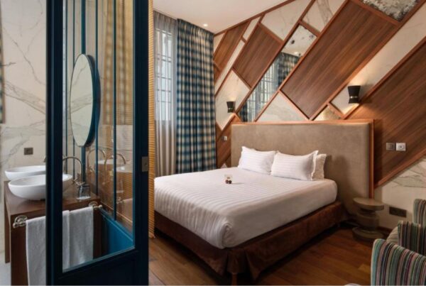 This is an image of a bedroom with an ensuite. There is a massive double bed in the middle and the walls have a cool criss cross pattern of wood, mirror and wallpaper.