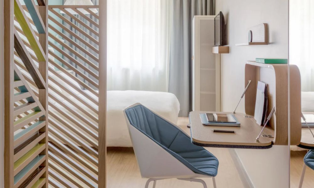 This is an image of a simple hotel room with a double bed, window and desk.