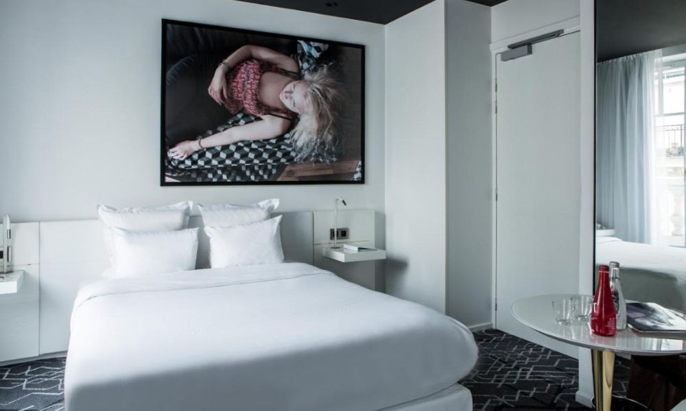 This is an image of a nice room with a minimalist white double bed, a painting on the wall and a small desk.