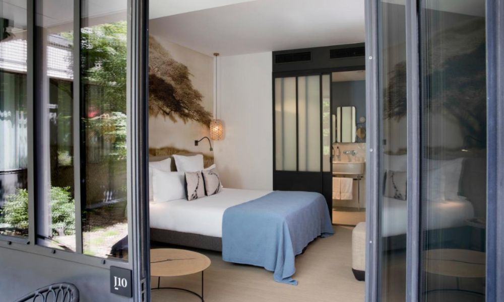 This is an image of an open-plan hotel room with a big king bed, a sitting area and a working area. The person is taking the shot from the outside of the room which what can only be assumed as the outdoor balcony or terrace.