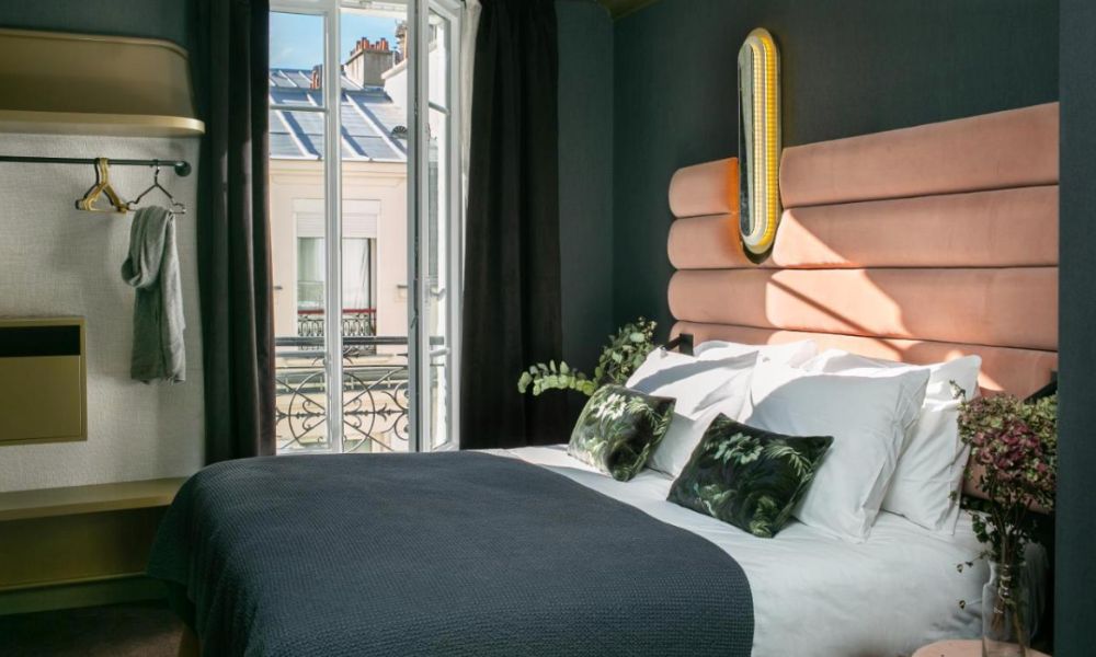 This is an image of a minimalist hotel room with a large wardrobe, big window, double bed and velvet bed head.