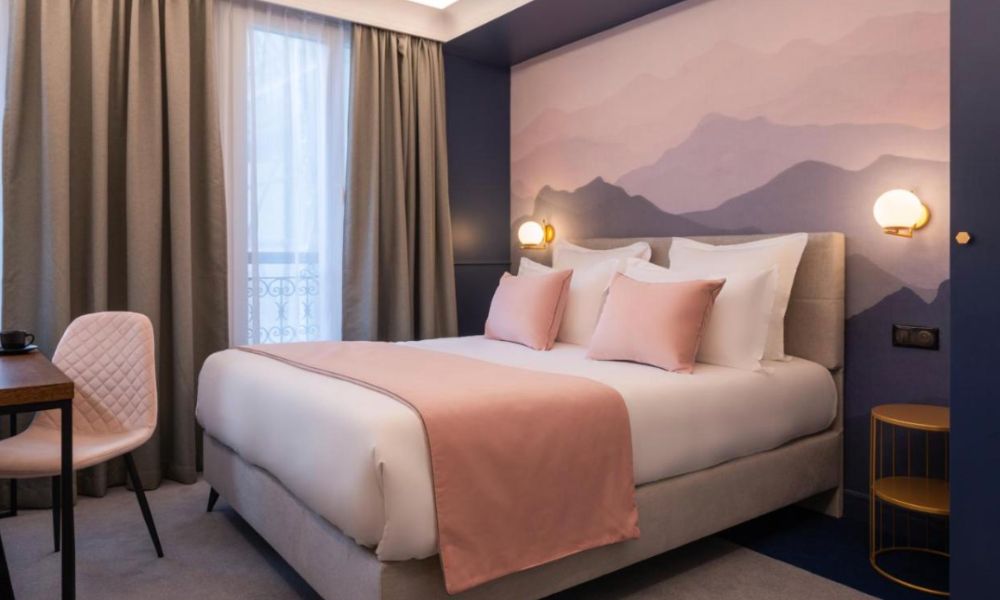 This is an image of a lovely room with a feature wall of mountainous views and a double bed in the centre. There is also a desk off to the side.