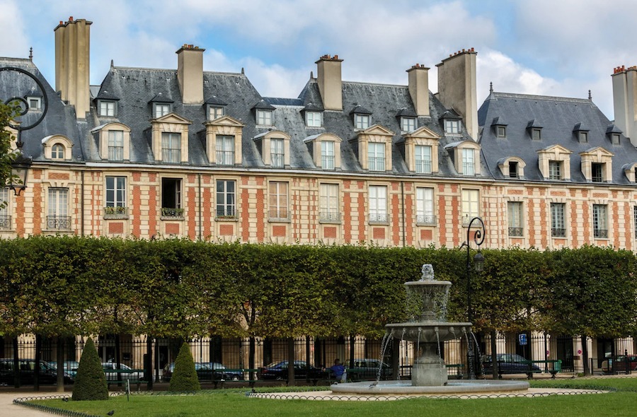This is an image of the outside of a very grand and big building with a beautiful park and water fountain in front.