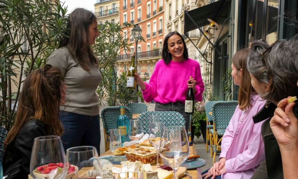 This is an image of a tour group sitting together with a waitress holding up wine bottles.