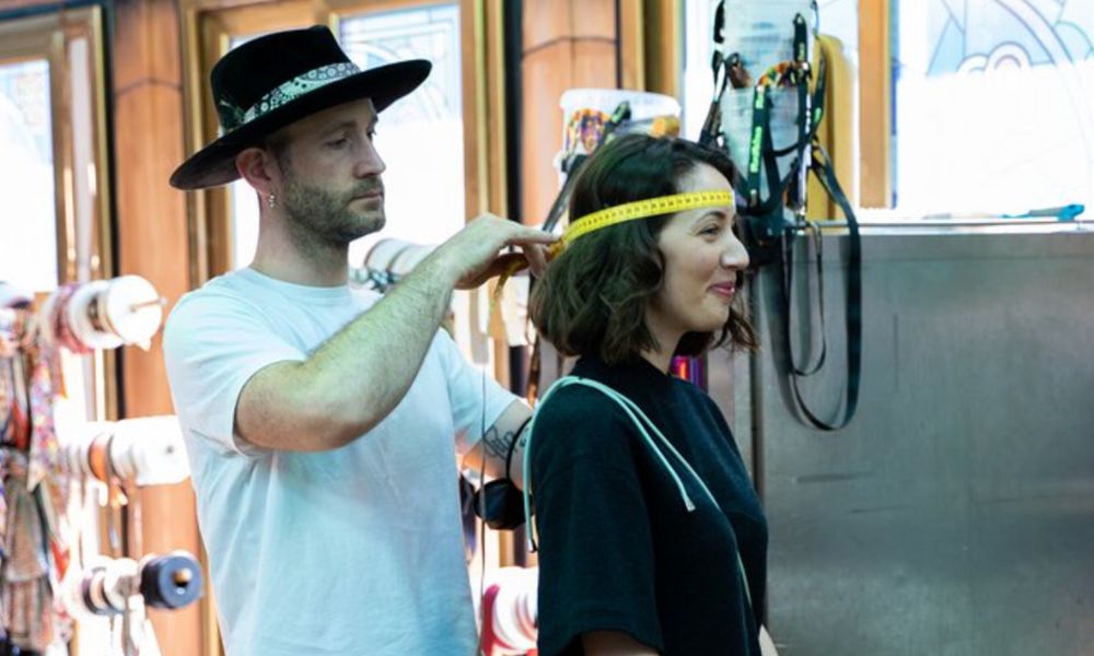 This is an image of a man measuring a lady's head to make hats.