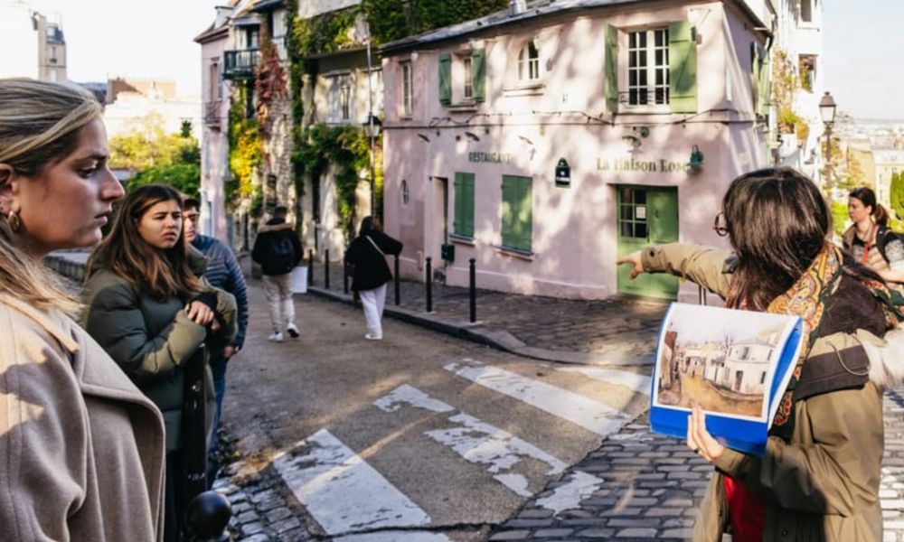 This is an image of a tour group looking at the famous pink restaurant 'La Maison Rose' on a hill in Montmartre.