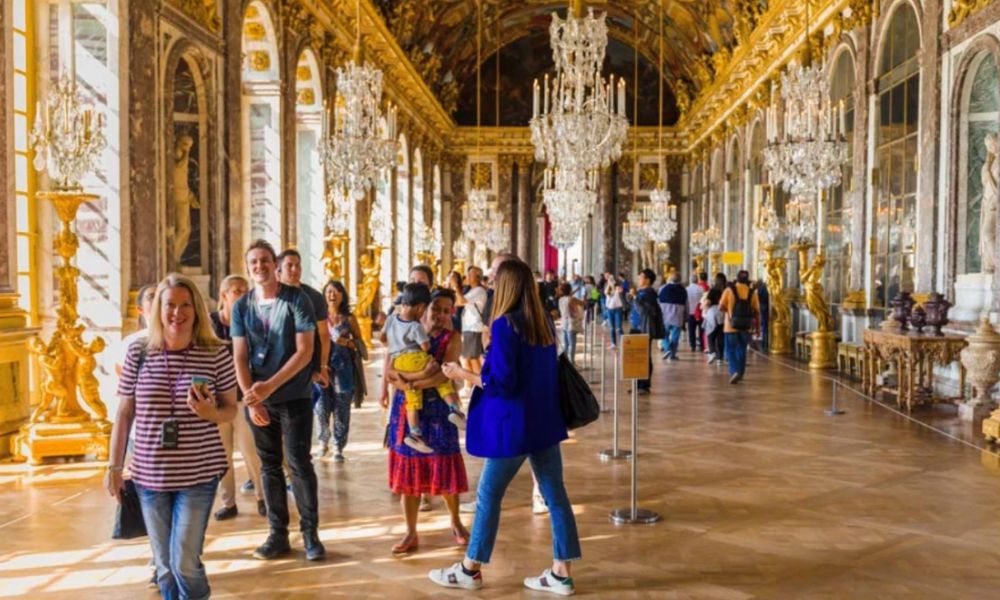 This is an image of people walking around the Versailles gold room with lots of detailing and chandeliers.