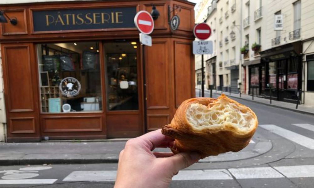 This is an image of a person holding up a crossaint in front of a bakery.