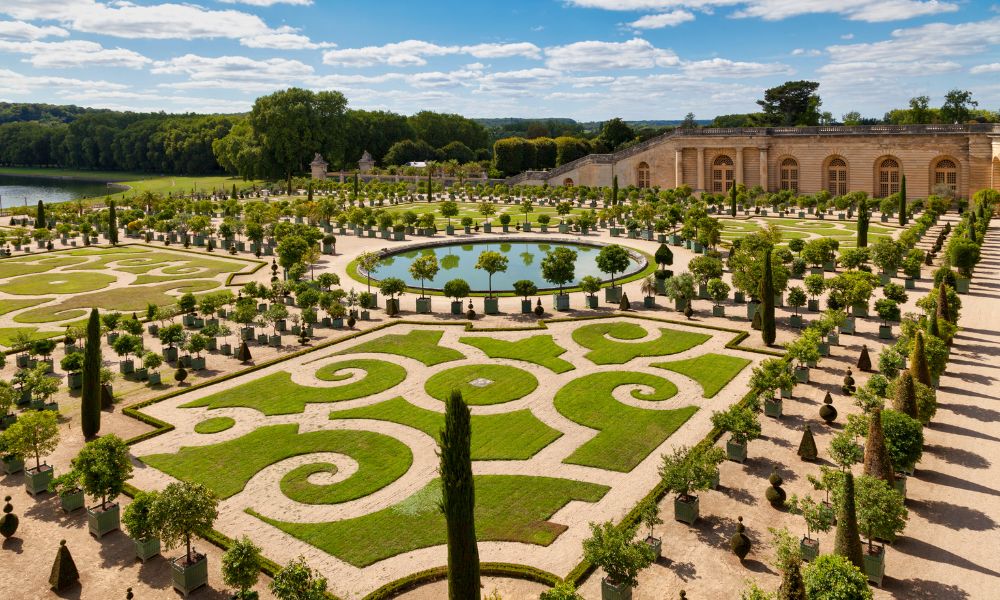 Things you should know before visiting Paris: This is an image of the gardens at the Palace of Versailles with greenery and a pond in the middle.